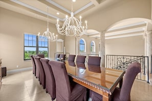 Uma ampla área de jantar com uma grande mesa de vidro, várias cadeiras e um candelabro.