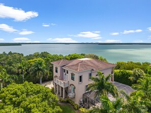 A two-story house with a red-tiled roof, surrounded by lush greenery and a view of a large body of water.