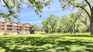 A grassy courtyard with trees and a row of multi-story buildings with balconies. - Poolside Perch | Sleeps 6 | Pet-Friendly (New Braunfels)