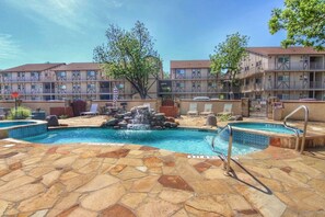 A hotel pool with a waterfall feature, lounge chairs, and a stone-tiled deck. - Poolside Perch | Sleeps 6 | Pet-Friendly (New Braunfels)