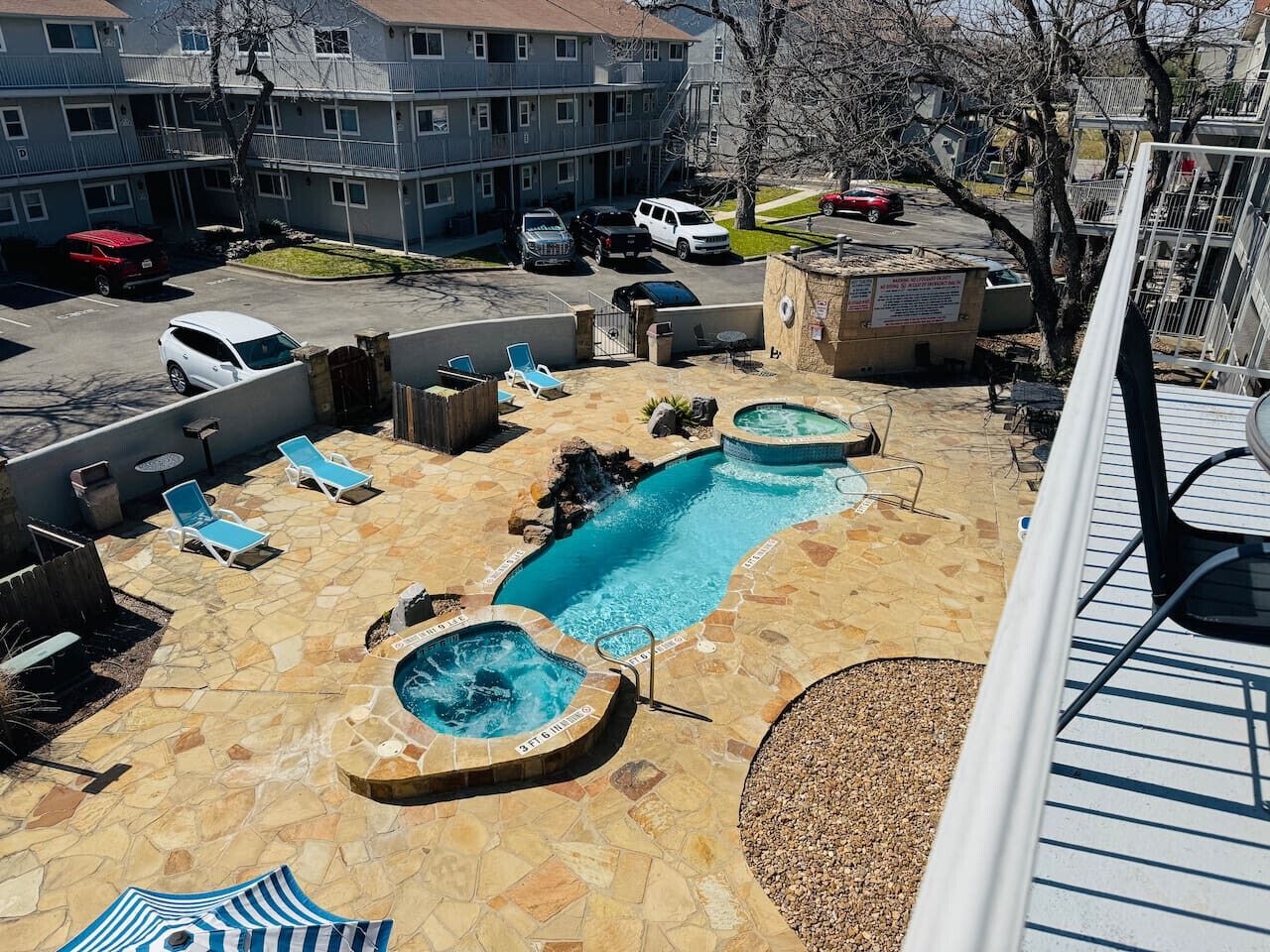 A rooftop pool area with two hot tubs and a small pool, surrounded by lounge chairs and a stone patio.