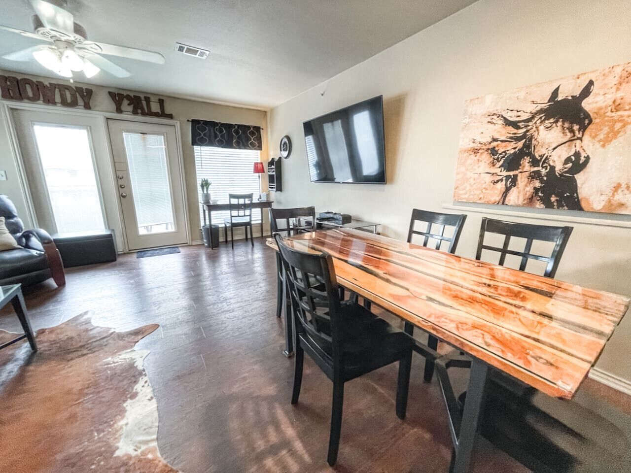 A dining area with a wooden table and chairs, a ceiling fan, and a mounted TV.