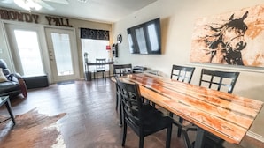 A dining area with a wooden table and chairs, a ceiling fan, and a mounted TV. - Poolside Perch | Sleeps 6 | Pet-Friendly (New Braunfels)