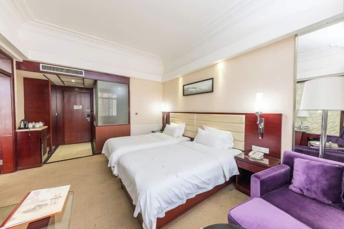 Una habitación de hotel con dos camas, un escritorio, un sofá morado y una mesita con un libro.
