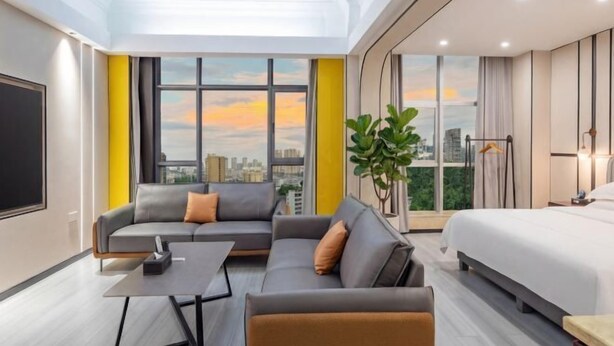 Una habitación de hotel moderna con una cama grande, un sofá, una mesita y un ventanal con vistas a la ciudad.