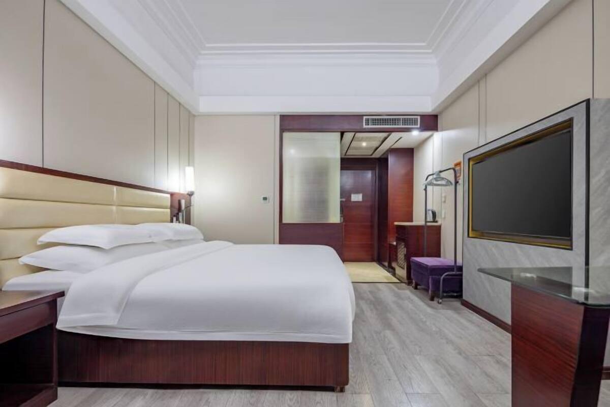 Una habitación de hotel con cama, escritorio, televisor y espejo.