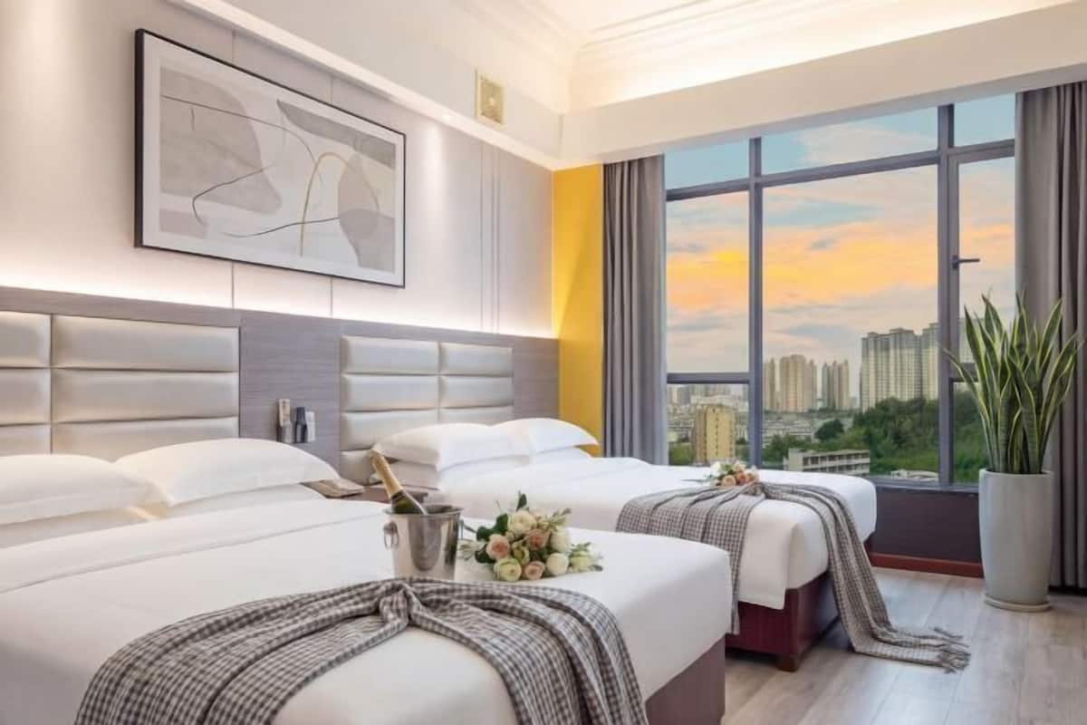 Habitación de hotel con dos camas, vista a la ciudad, un ventanal grande y diseño moderno.