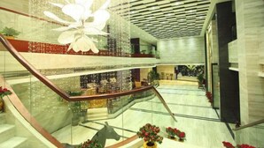 Un vestíbulo de hotel de varios niveles con una escalera de cristal, iluminación decorativa y plantas en macetas.