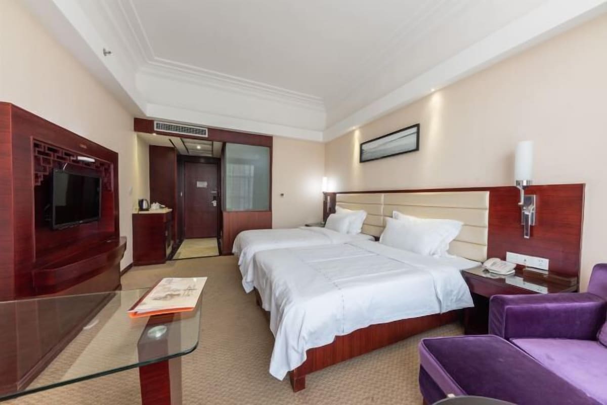 Habitación de hotel con dos camas, un televisor, un escritorio y un sillón púrpura.