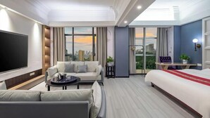 Habitación de hotel moderna con una televisión grande, un sofá, una cama y un balcón con vistas a la ciudad.