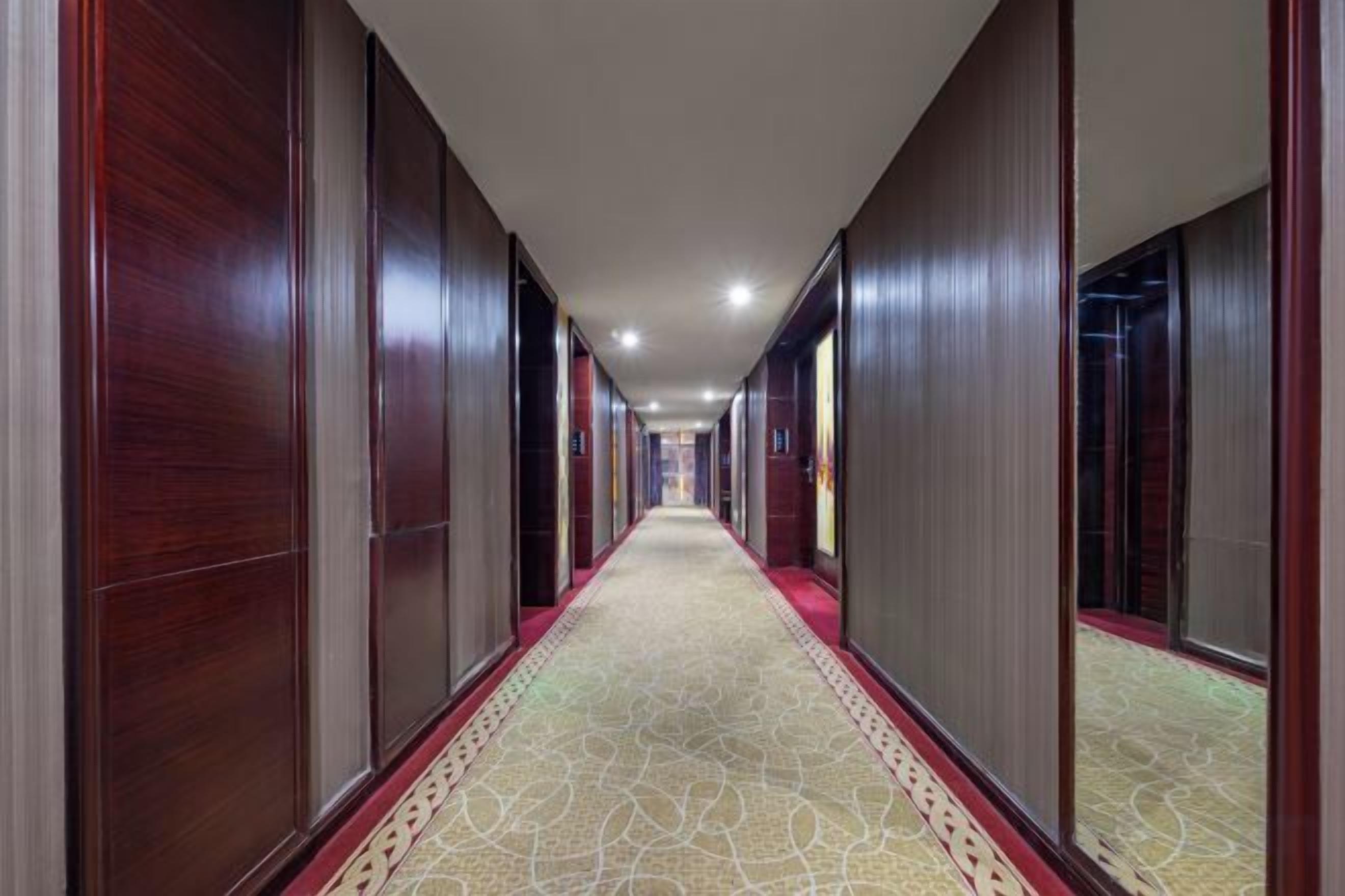 Ein Hotelkorridor mit Holzvertäfelung, einem gemusterten Teppich und einem roten Teppichrand.