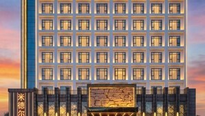Un moderno edificio de hotel con una cuadrícula de ventanas y una fachada de piedra en la parte inferior.