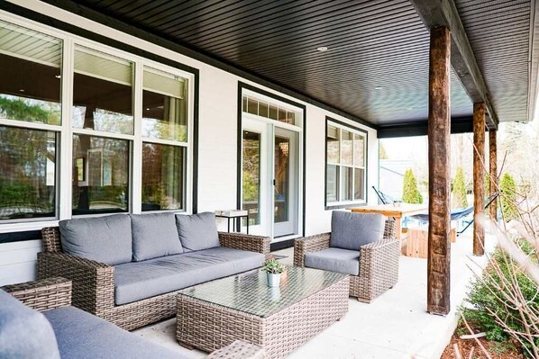 A covered outdoor seating area with wicker furniture and a glass coffee table.