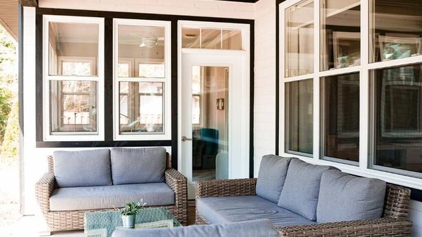 A covered outdoor seating area with wicker furniture and a glass door leading to an interior space.