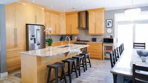 A modern kitchen with wooden cabinets, a stainless steel refrigerator, a granite countertop, and a bar stool seating area.
