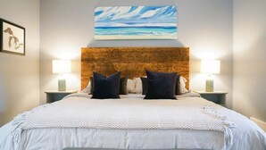 A bedroom with a wooden headboard, white bedding, two bedside lamps, and a framed picture on the wall.