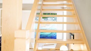 A wooden staircase with glass panels, leading to a room with a painting of a landscape.