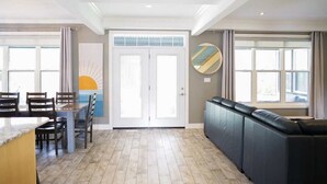 A spacious living area with a dining table, chairs, a sofa, and a large window.