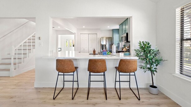 A modern kitchen with a central island, three bar stools, and a potted plant. - Cozy Home Near Seawall with Private Pool (Galveston)
