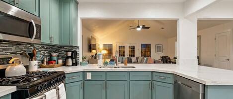 Una cocina con gabinetes verde azulado, una estufa, un microondas y un lavavajillas.