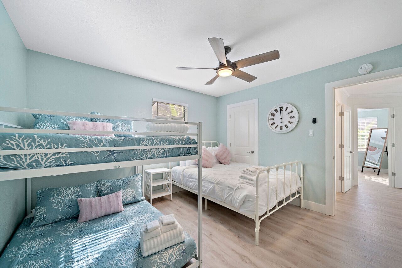 A bedroom with bunk beds, a ceiling fan, a clock, and a door leading to another room.