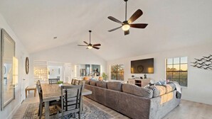 A spacious living area with a large sofa, a dining table, and ceiling fans. - Cozy Home Near Seawall with Private Pool (Galveston)