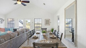 A dining area with a wooden table set for four, a ceiling fan, and a large window. - Cozy Home Near Seawall with Private Pool (Galveston)