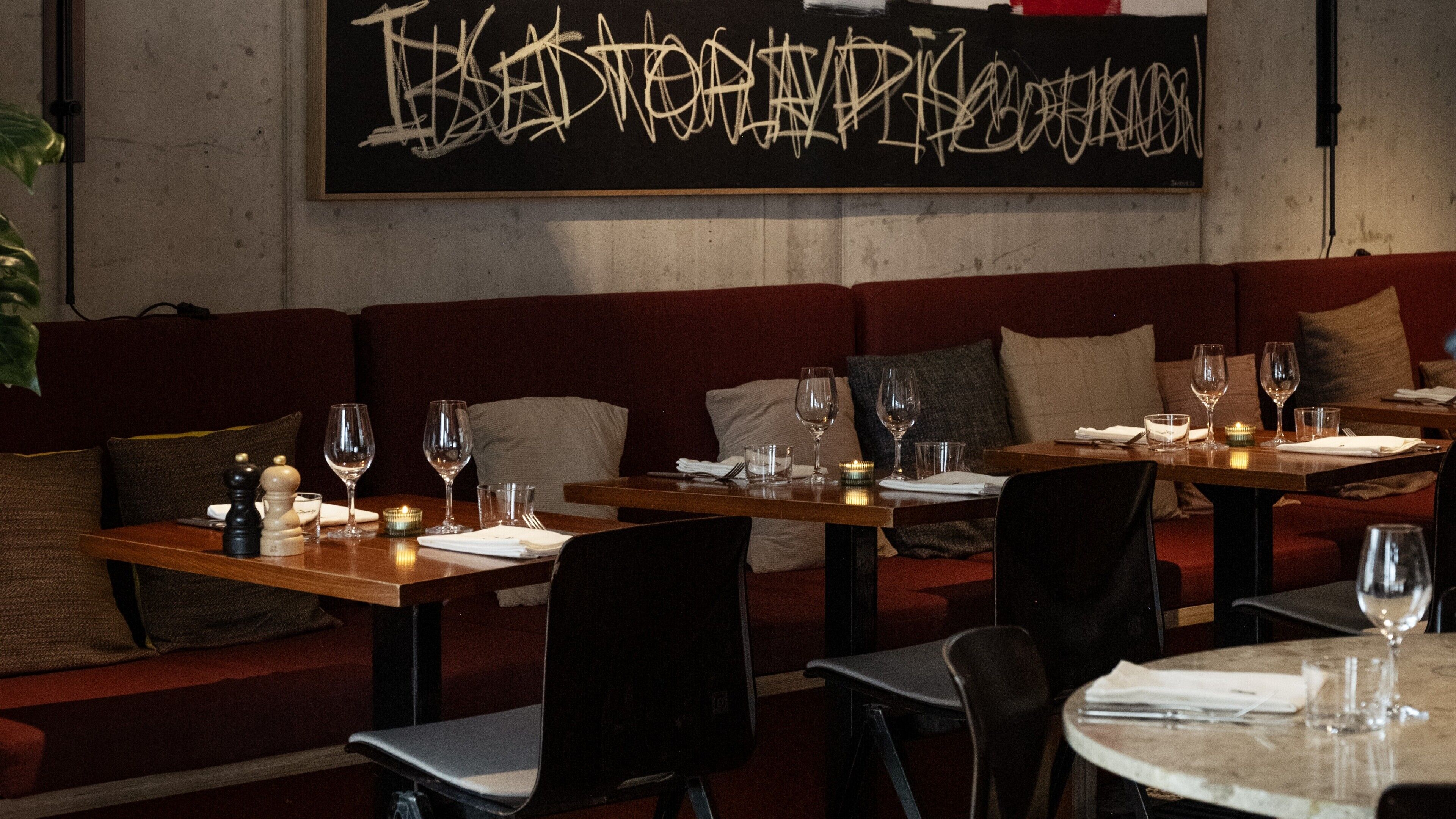 A restaurant interior with wooden tables, red cushioned seating, and a graffiti wall.