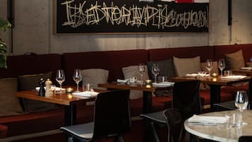 Interior de restaurante com mesas de madeira, assentos acolchoados vermelhos e uma parede com grafite.