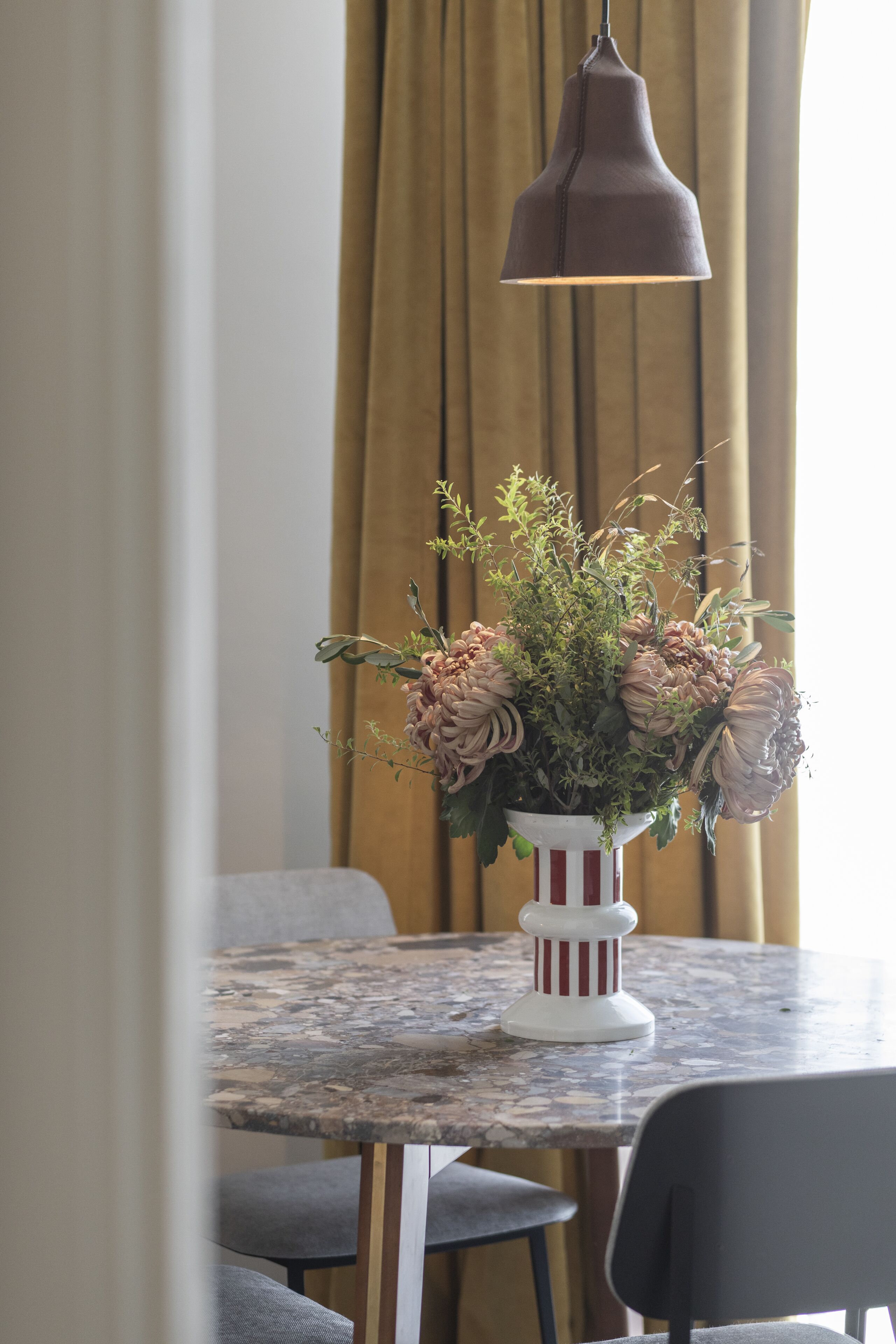 Ein Tisch mit einer Blumenvase, einer hängenden Pendelleuchte und einem gestreiften Kerzenhalter.