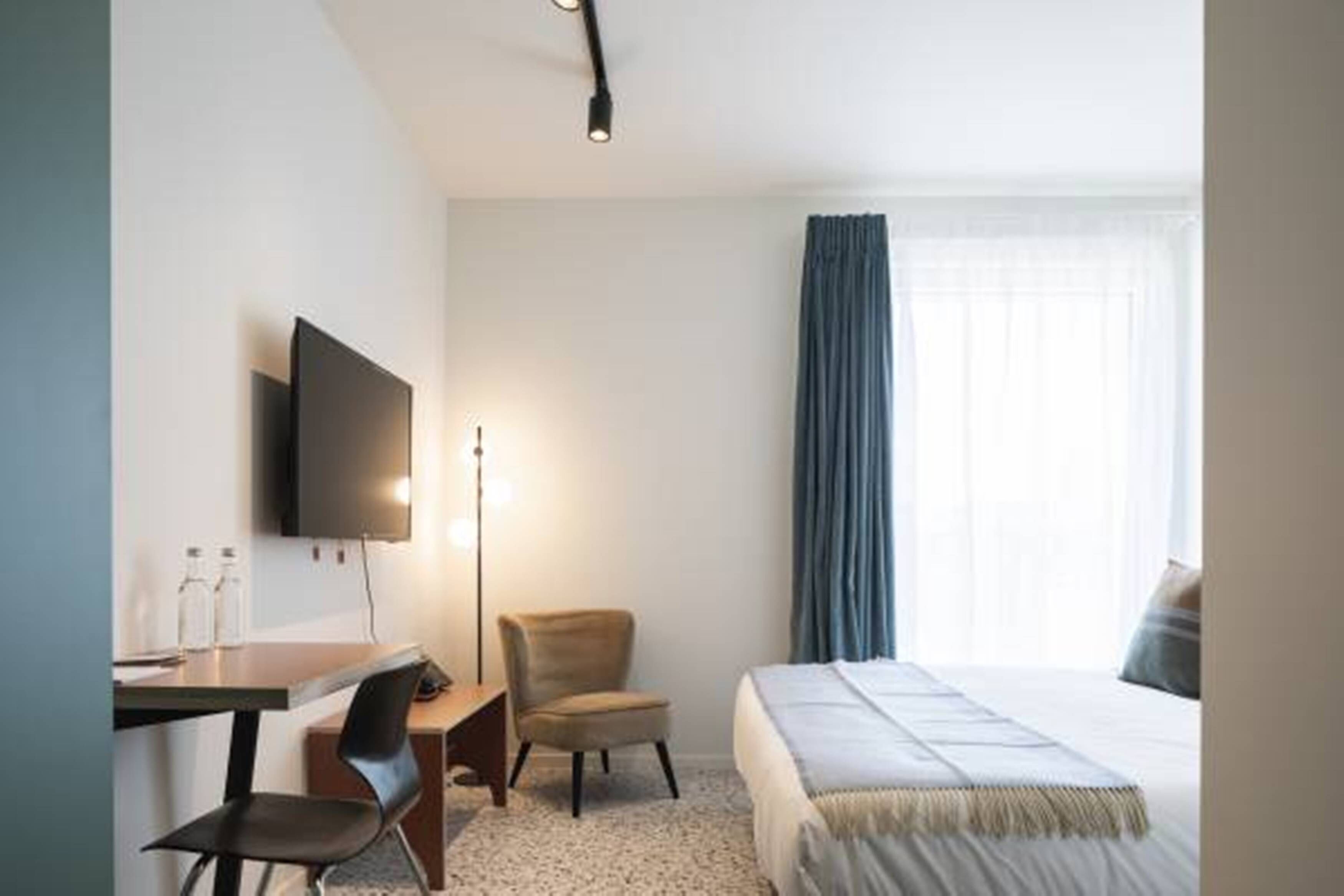 A hotel room with a bed, a desk with a chair, a flat-screen TV, and a lamp.