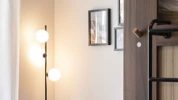 A dormitory room with a bunk bed, a desk, a chair, and a wall-mounted lamp.