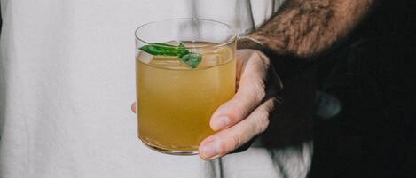 A person holding a glass of amber-colored liquid with a green leaf garnish.