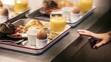 A breakfast tray with eggs, toast, and orange juice on a stainless steel counter.