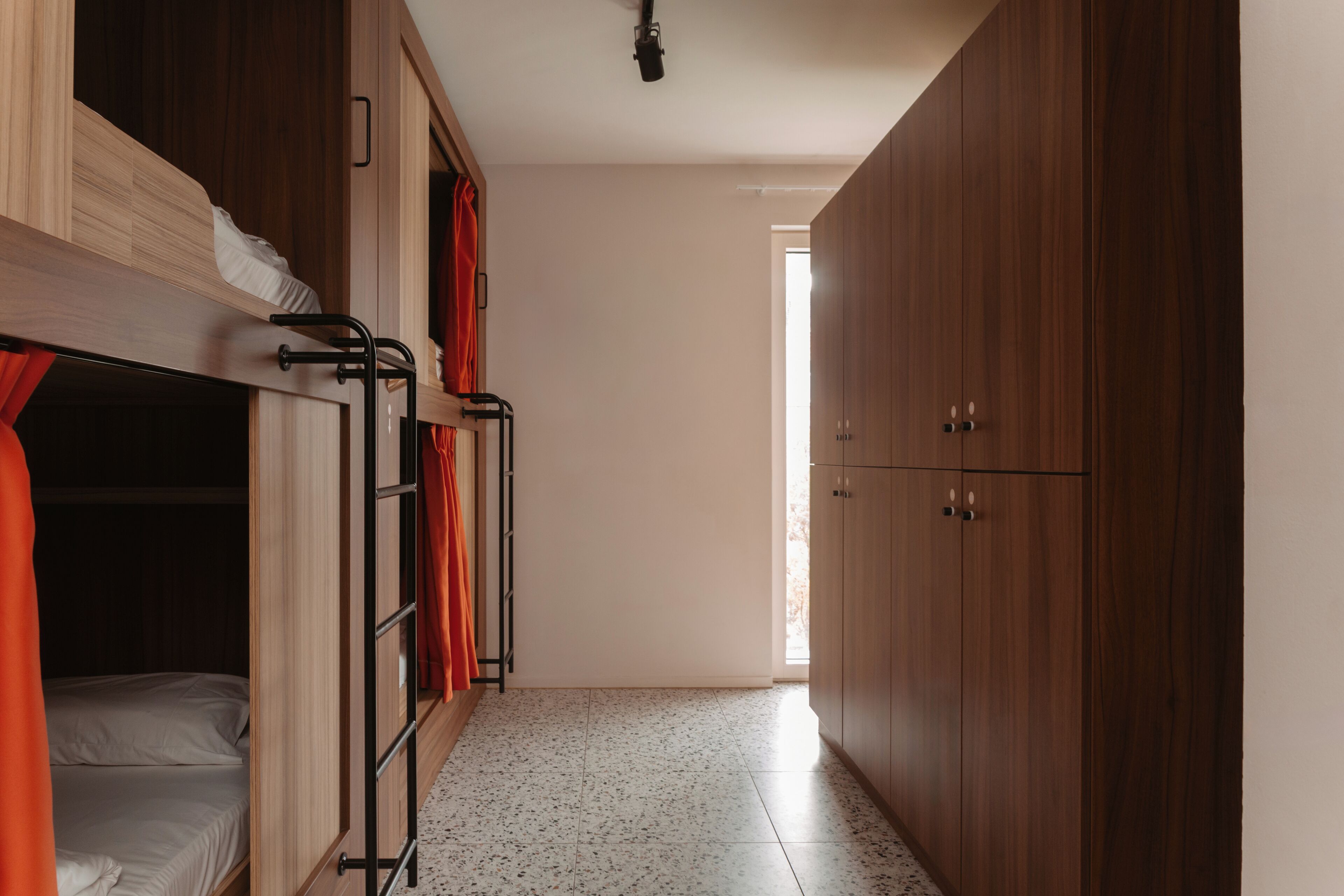 A dormitory room with bunk beds, a wardrobe, and a tiled floor.