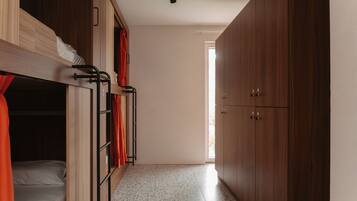 A dormitory room with bunk beds, a wardrobe, and a tiled floor.