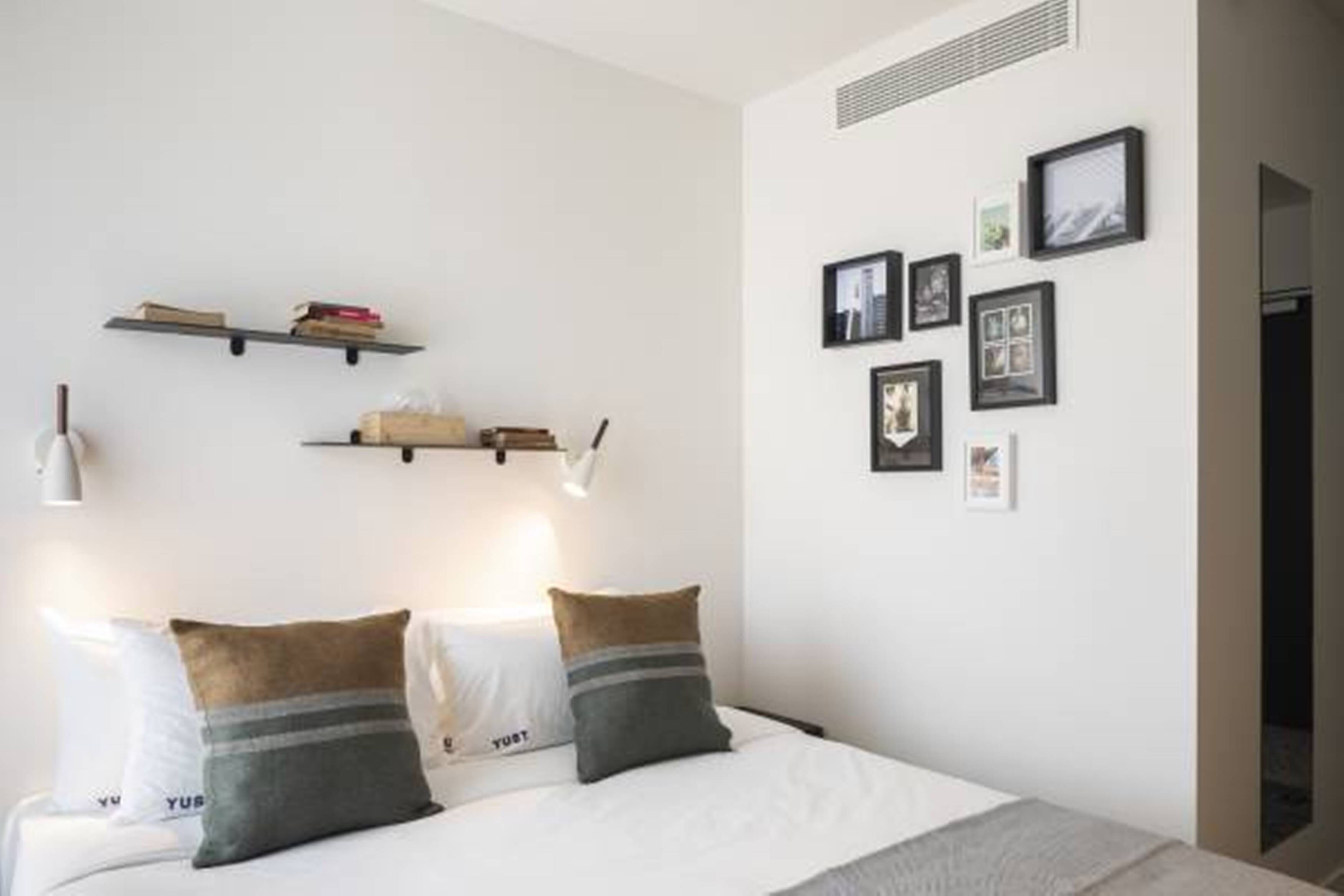 A minimalist bedroom with a bed, two bedside tables, and wall-mounted shelves with books and pictures.
