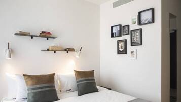 A minimalist bedroom with a bed, two bedside tables, and wall-mounted shelves with books and pictures.