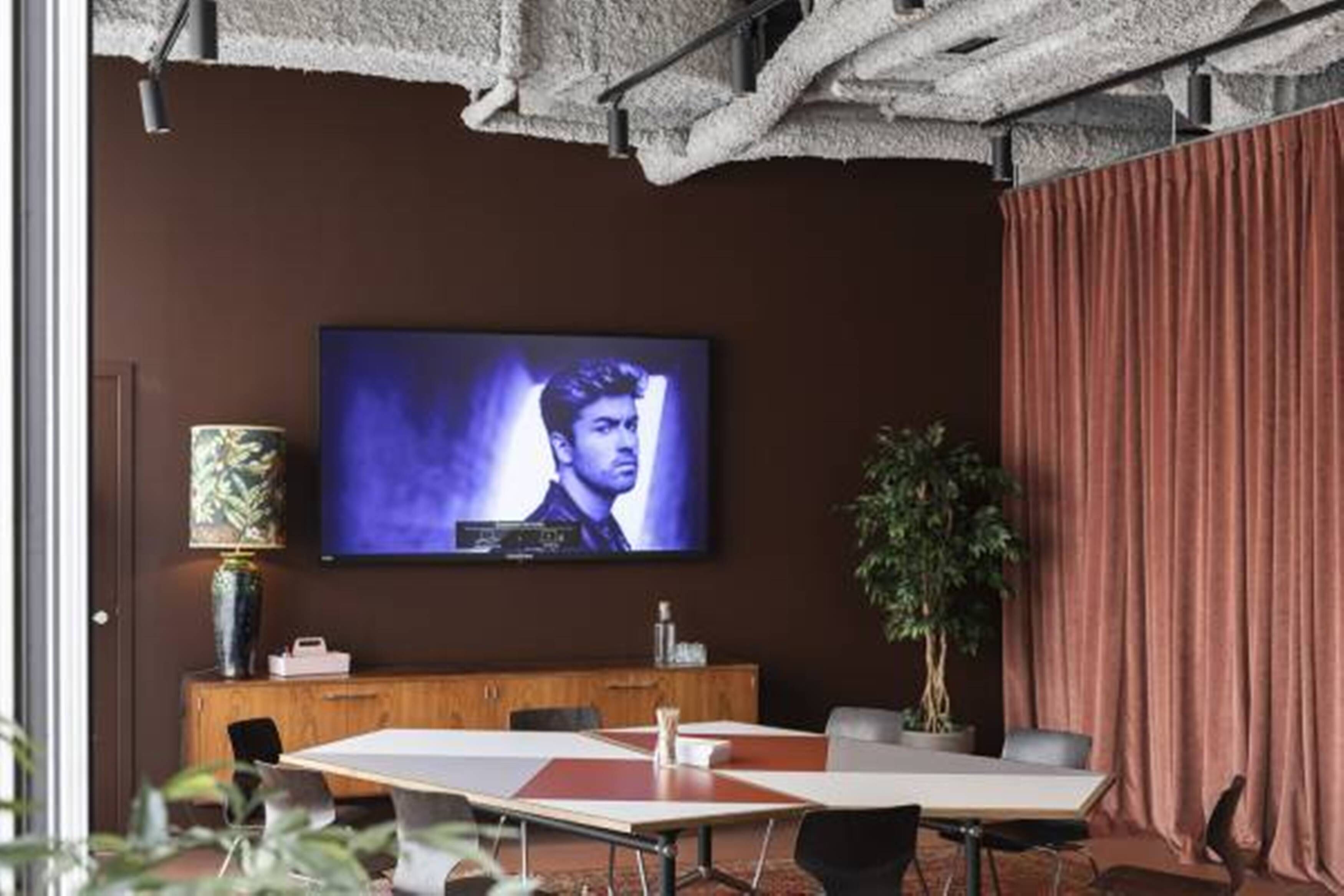 Uma sala de conferências com uma grande TV de tela plana na parede, um armário de madeira e um vaso de planta.
