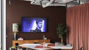 Uma sala de conferências com uma grande TV de tela plana na parede, um armário de madeira e um vaso de planta.