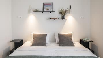 Een moderne slaapkamer met een bed, twee nachtkastjes, een wandplankje, een lijst met een afbeelding en twee wandplanken met decoratieve objecten.