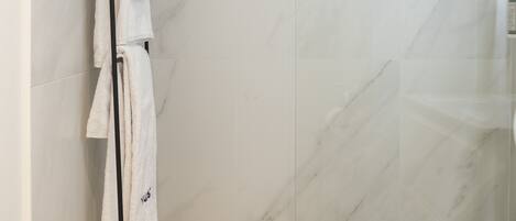 Un baño moderno con cabina de ducha de vidrio, paredes de mármol y un toallero negro.