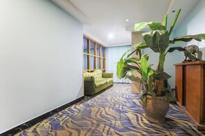 Un pasillo con alfombra estampada, un sofá verde, una planta en maceta y un aparador de madera.