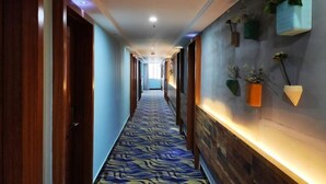 Un pasillo de hotel con alfombra estampada, puertas de madera y macetas colgantes en la pared.