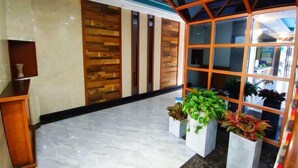 Vestíbulo con piso de mármol, paneles de madera y un gran ventanal con plantas.
