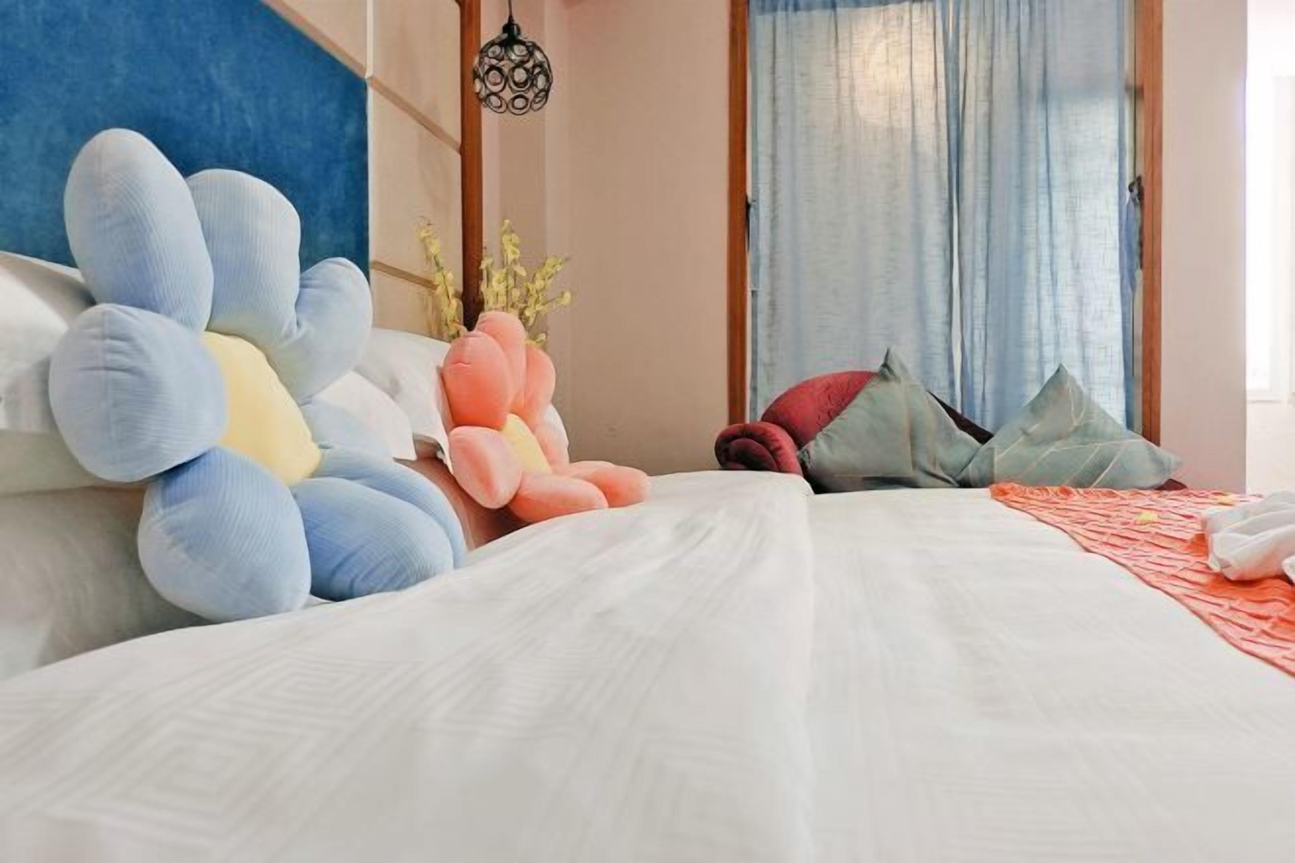 A neatly made bed with a white comforter, a blue and pink plush toy, and a few pillows in a room with a blue accent wall and a hanging light fixture.