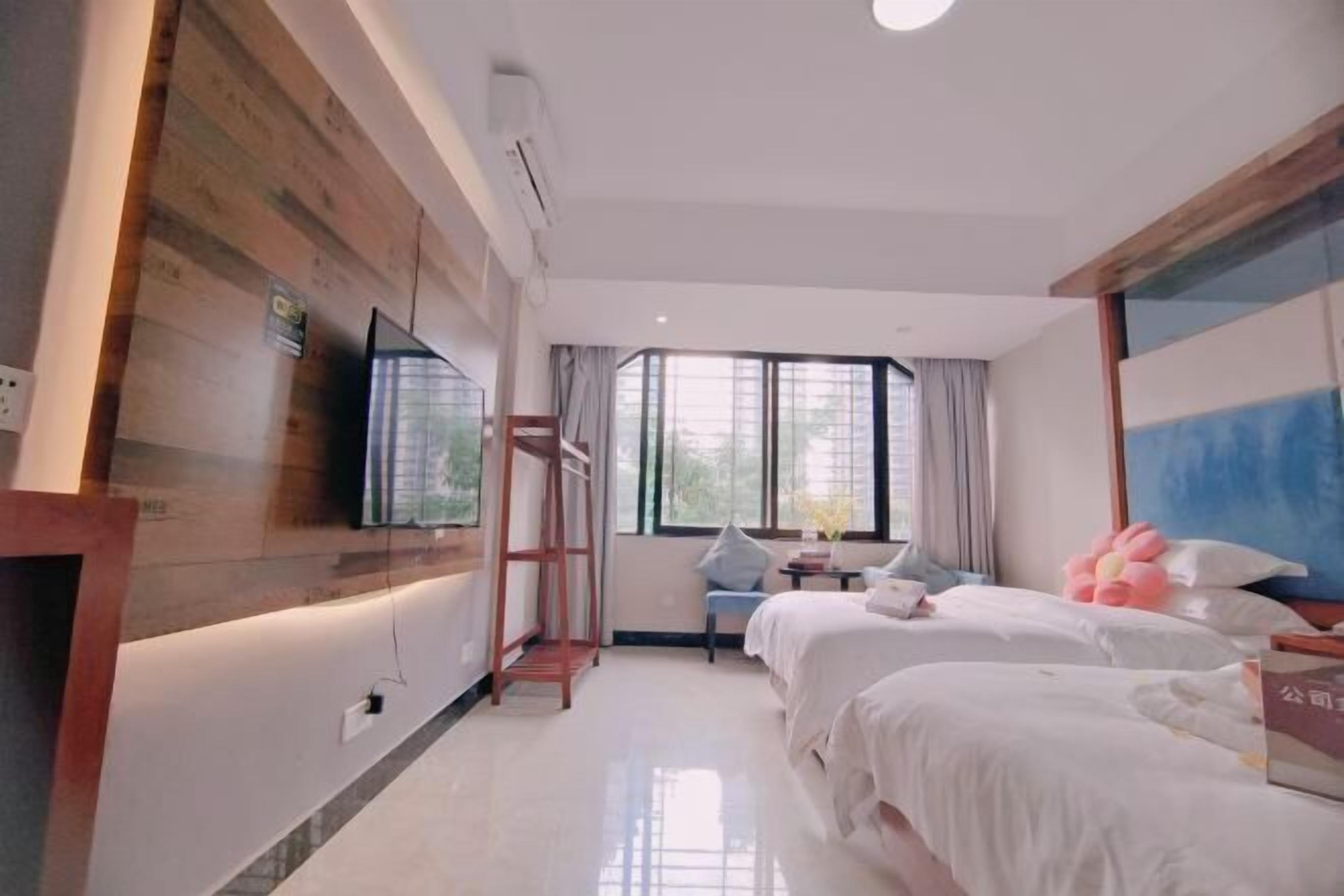 A hotel room with two beds, a TV, a window with curtains, and a wooden accent wall.