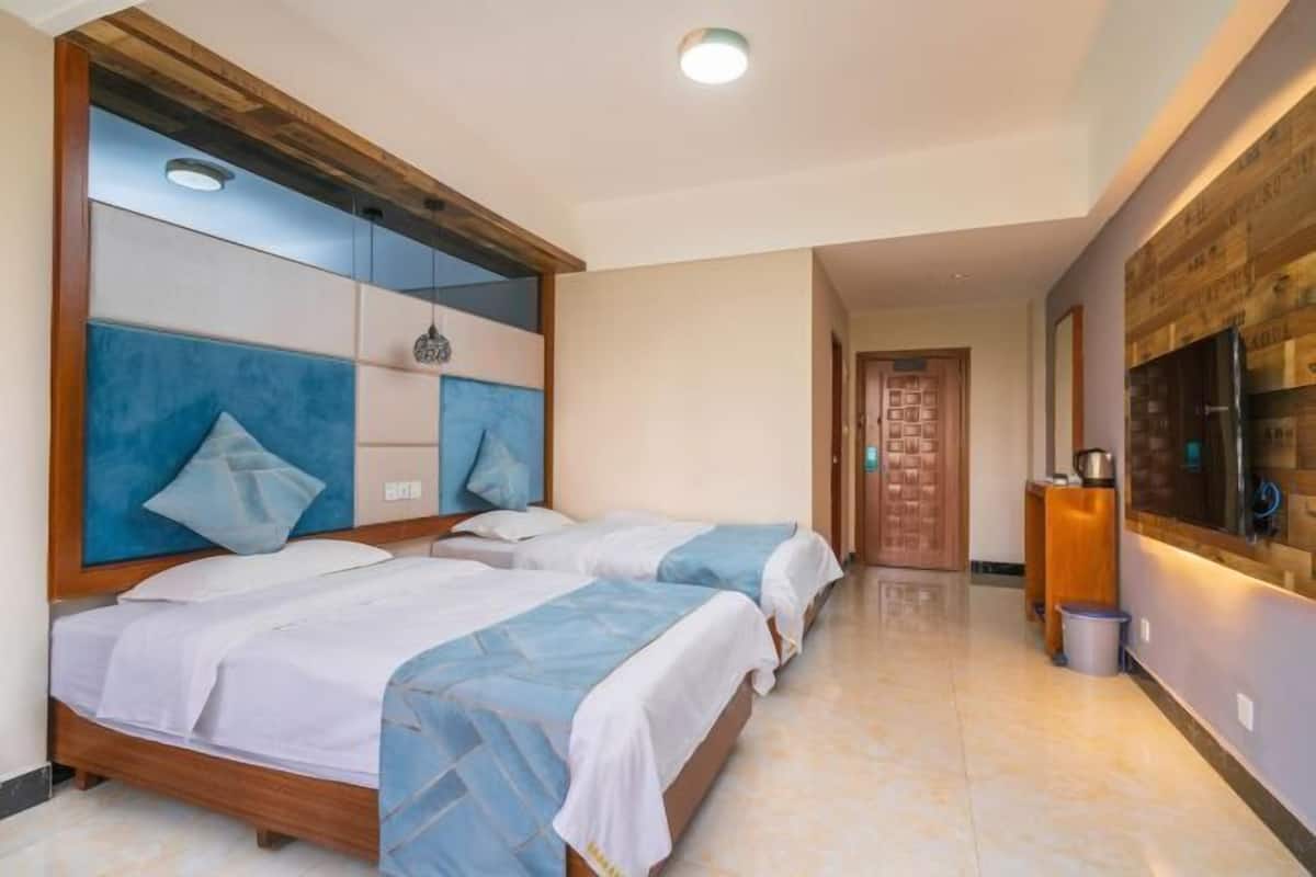 A hotel room with two beds, a wooden headboard, a tiled floor, a wooden door, and a wall-mounted TV.