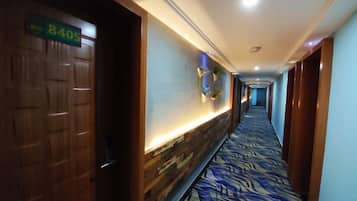 Corredor de hotel com carpete estampado, portas de madeira e acesso a um quarto.