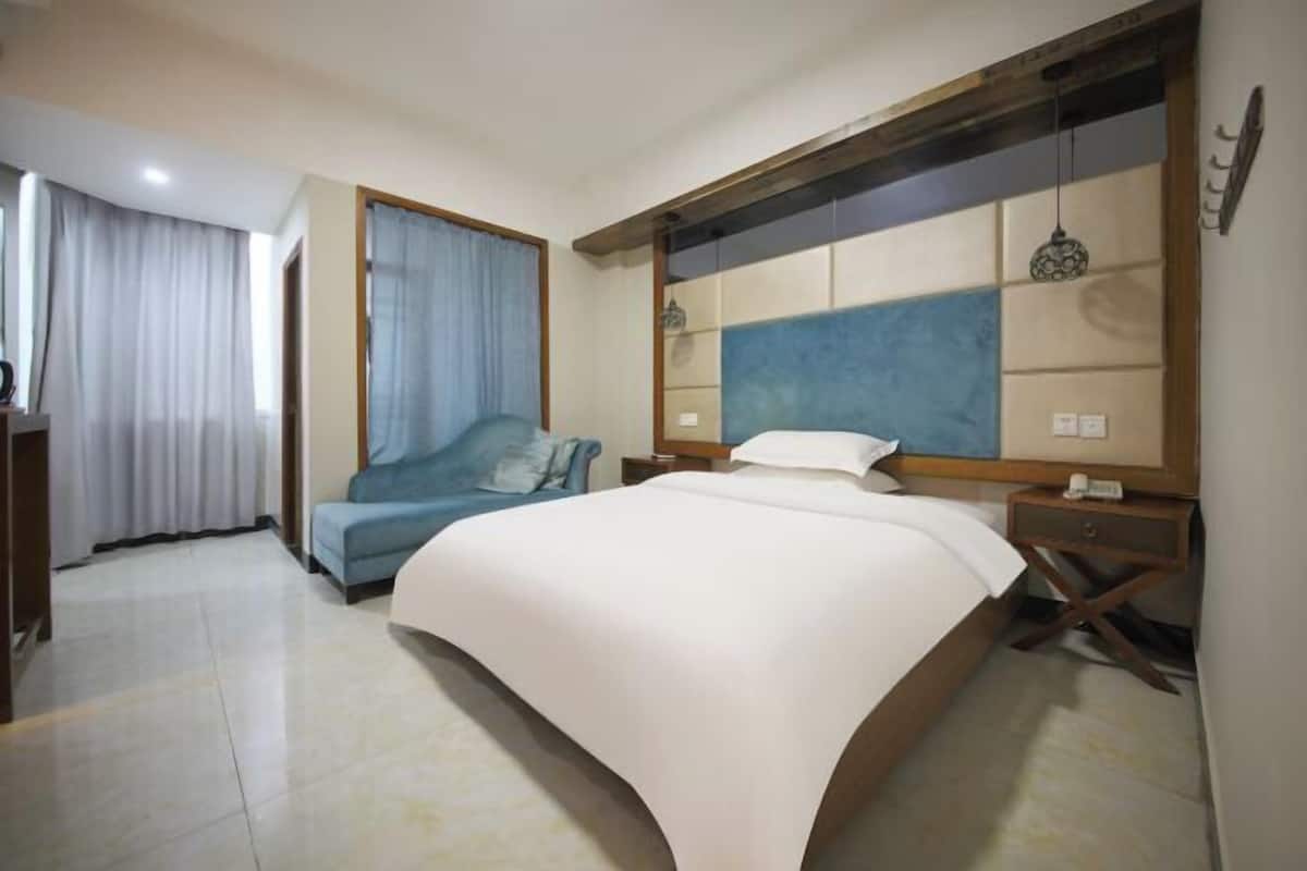 A modern hotel room with a large bed, a sofa, a desk, and a window with curtains.